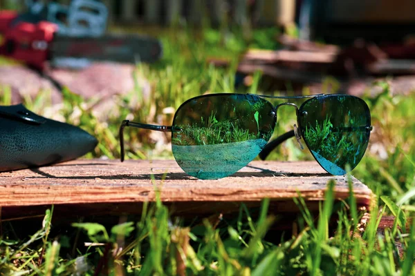 Blue sunglasses on a background of green grass and a power saw — 스톡 사진