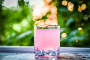 Ahşap masada pembe kokteylli cam bardak.