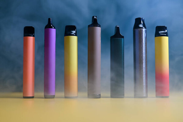 multicolored vape electronic cigarettes on dark green background in smoke