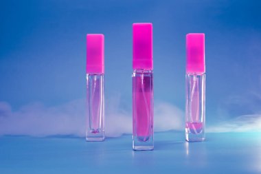 Kadın parfümü şeffaf bir şişede, eflatun arkaplanda dumanlı.