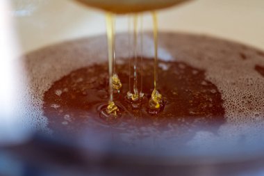 Altın nektarla doldurulmuş altıgen bal peteklerinden bir damla bal damlıyor. Bal peteği yaz kompozisyonu. Doğal bal damlası, balmumu çerçeveli arı damlası. Bal damlası bal damlatıyor bal peteğine.