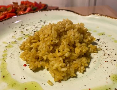 Köri pilavı bir tabakta, masada, bir kafede, bir restoranda sıcak bir ışıkta, lezzetli bir yemekte. Kızartma tavasındaki kırmızı biberlerin arka planında. Köri, Hindistan kökenli bir yemektir.