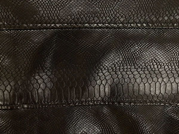 Dark brown leather material, part of clothes, leather jacket, large seams. Artificial leather looks like a snake skin, a crocodile