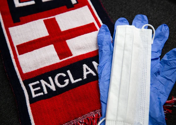 White mask and blue latex gloves, next to the scarf of a Great Britain football fan with the inscription England on it