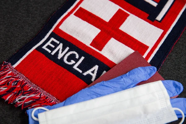 White mask and blue latex gloves, document, next to the scarf of a Great Britain football fan with the inscription England on it
