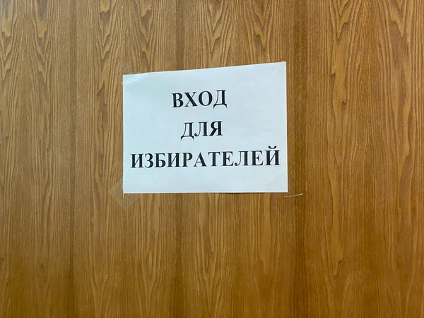 Mari El, Russland - 16. September 2021: An einer Holztür oder -wand hängt ein Blatt weißes Papier mit einer Inschrift auf Russisch - Eingang für Wähler. Wahl zur Staatsduma am 19. September 2021 — Stockfoto