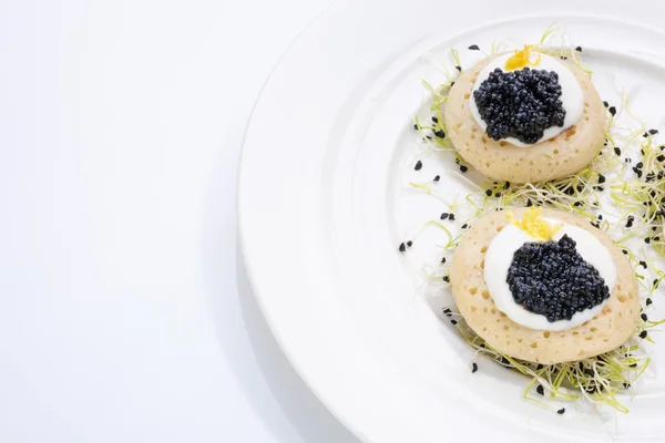 Caviar de pescado frito en panqueques con crema y una cama de brotes de puerro. comida en un plato blanco. espacio para texto . — Foto de Stock