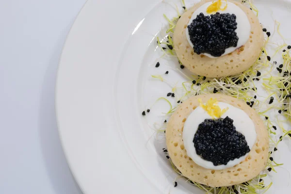 Caviar de pescado frito en panqueques con crema y una cama de brotes de puerro. comida en un plato blanco. espacio para texto . — Foto de Stock