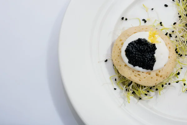 Caviar de pescado frito en panqueques con crema y una cama de brotes de puerro. comida en un plato blanco. espacio para texto . — Foto de Stock