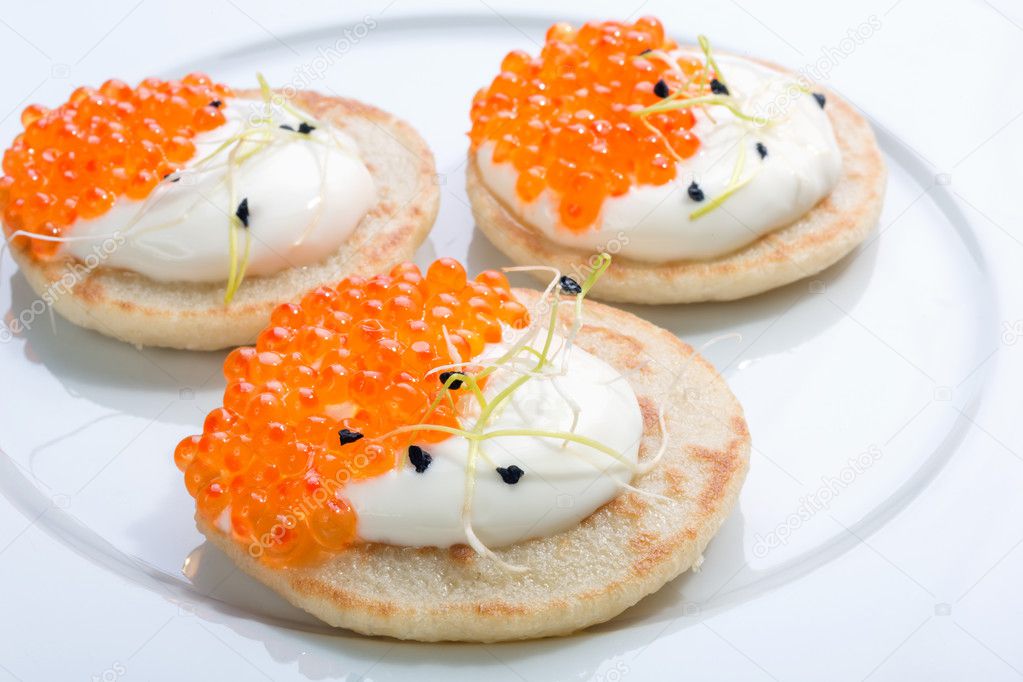 red fish caviar on pancakes with cream. food on a white plate. space for text.