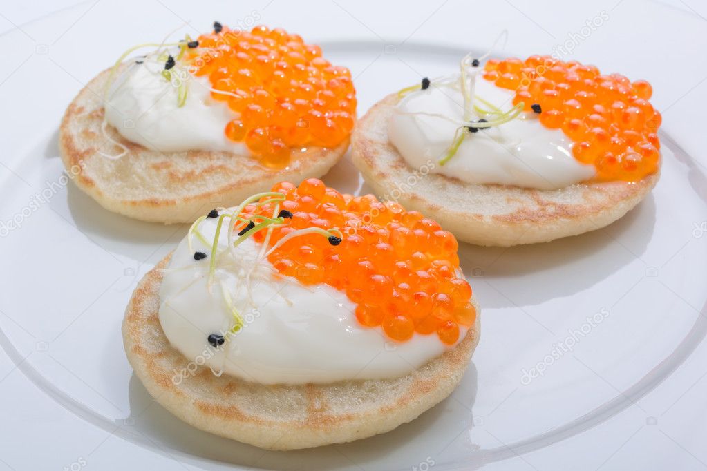 red fish caviar on pancakes with cream. food on a white plate. space for text.