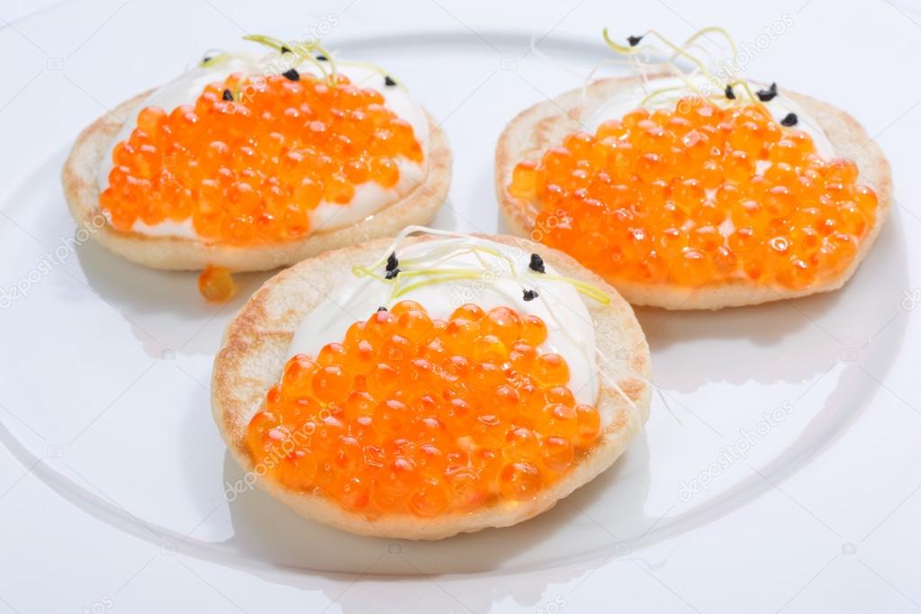 red fish caviar on pancakes with cream. food on a white plate. space for text.