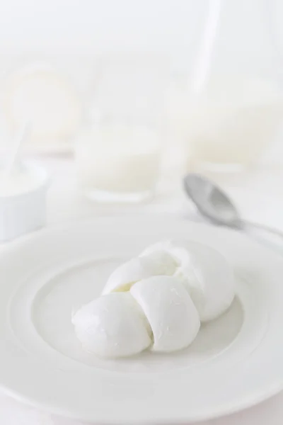 En bit ost i form av flätor på en vit platta. Foto mejeriprodukt i en ljus nyckel. stilleben i vitt. Traditionell italiensk produkt — Stockfoto