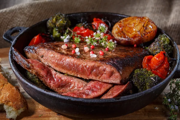 Sığır eti biftek pişmiş sebzeler bir dökme demir tava üzerinde. düşük anahtar yiyecek natürmort. bir fincan Avrupa mutfağı. rustik tarzda gıda