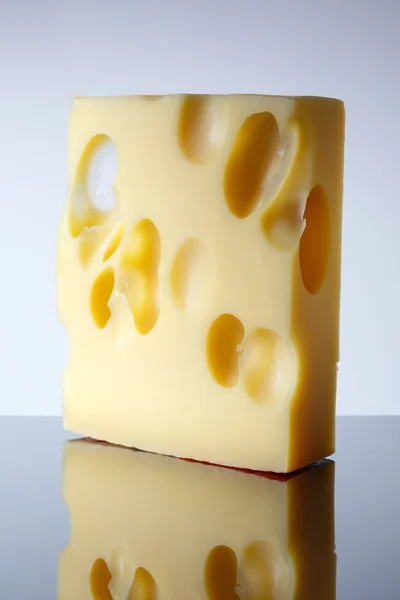 En bit ost med stora hålen på ljus bakgrund med en toning. Emmentaler. — Stockfoto