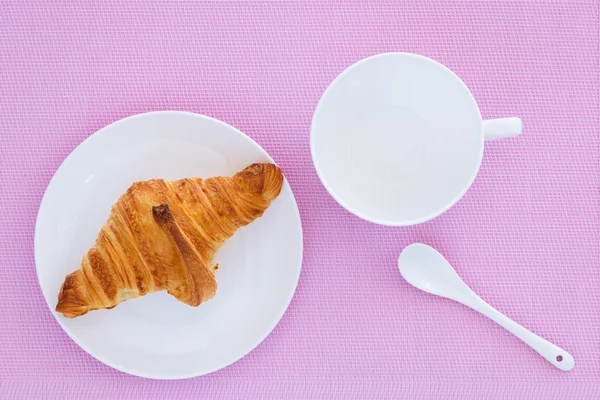 Croissant em uma placa branca e fundo rosa — Fotografia de Stock