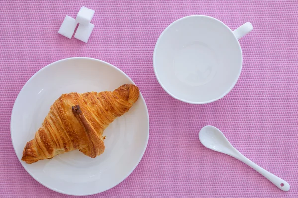 Croissant em uma placa branca e fundo rosa — Fotografia de Stock