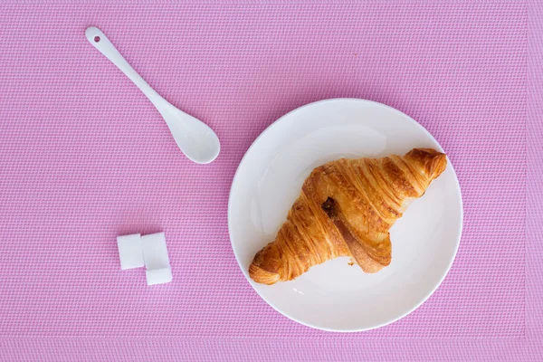 Croissant on a white plate and pink background — Stock Photo, Image