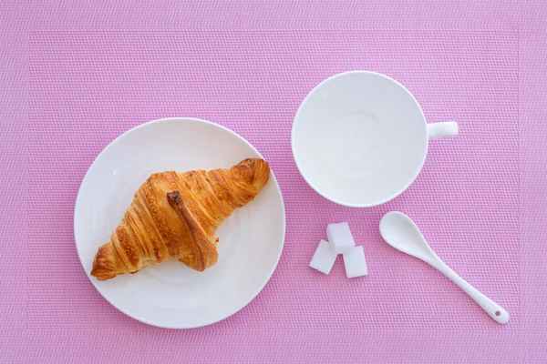 Croissant em uma placa branca e fundo rosa — Fotografia de Stock