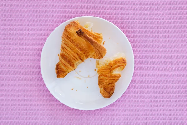 Croissant em uma placa branca e fundo rosa — Fotografia de Stock