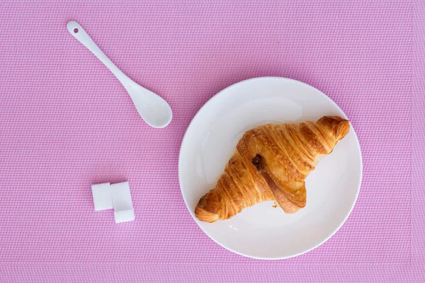 Croissant auf weißem Teller und rosa Hintergrund — Stockfoto