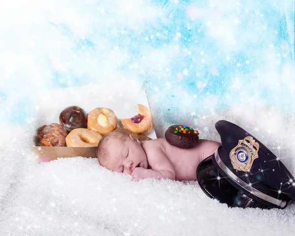 baby sleeping next to a box of donuts next to a police hat