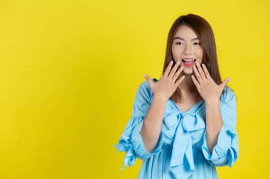 Şok olmuş bir kadın, sarı arka planda elleri olan ağzı kapatıyor.