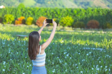 Çiçek bahçesinde fotoğraf çekmek için cep telefonu kullanan bir kadın..