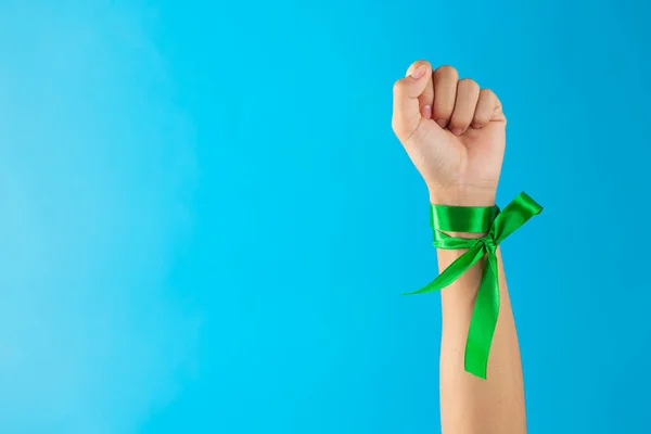 World Mental Health Day;green ribbons tied at the wrist on blue background