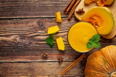 Bir bardak balkabağı suyu ve ahşap zeminde doğranmış çiğ balkabağı yeri.