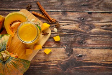 Bir bardak balkabağı suyu ve tahta kesme tahtasının üzerinde doğranmış çiğ balkabağı yeri.