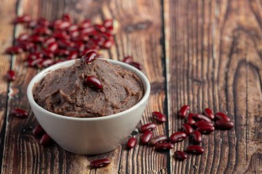 Tahta zeminde beyaz kâse içinde tatlı kırmızı fasulye ezmesi.