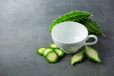 empty cup put next to raw sliced bitter gourd on dark floor