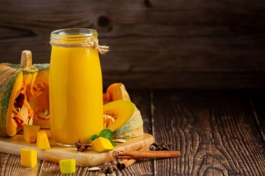 Bir bardak balkabağı suyu ve tahta kesme tahtasının üzerinde doğranmış çiğ balkabağı yeri.