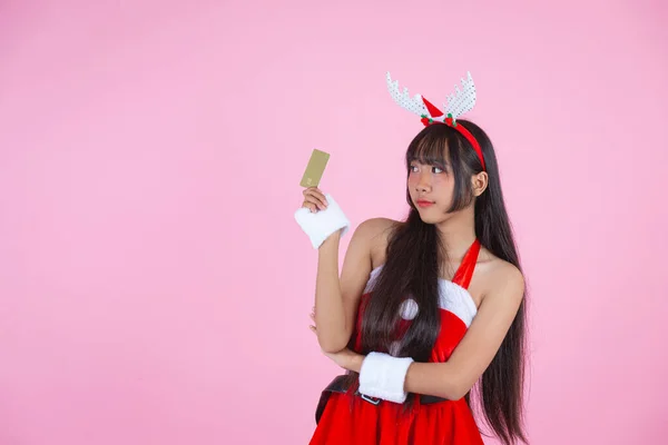 ピンクの背景にクレジットカードを持っているクリスマスの衣装のかわいい女の子 — ストック写真