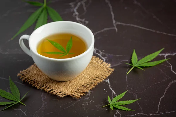 a cup of hemp tea with hemp leaves put on black marble floor