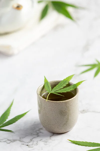 a cup of hemp tea with hemp leaves put on white marble floor