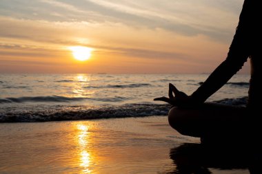 Siluet kadın gün batımında plajda yoga yapıyor..