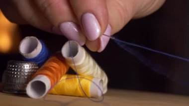 Renkli iplikli makaralar. Kadınların parmakları iğne deliğinden geçen bir ipliği gerer. Yakın çekim..