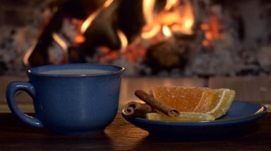 Çay, içki. Bir adam, şömine ateşinin arka planında bir içecekle bir çay kaşığı sütü karıştırıyor. Yakın çekim..