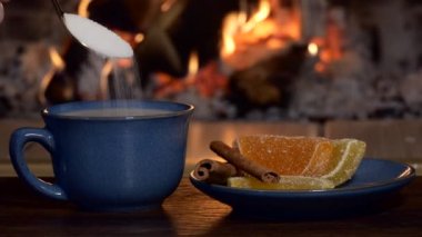 Holiday, drink. A man pours a teaspoon of sugar into a cup of tea and milk and stirs it against the background of christmas decorations and the firelight. Close-up shooting.