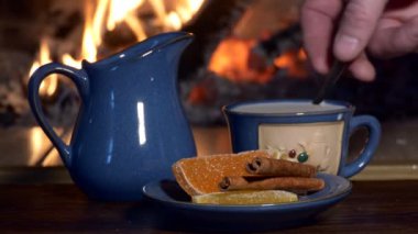 Çay, içki. Bir adam, şömine ateşinin arka planında bir içecekle bir çay kaşığı sütü karıştırıyor. Yakın çekim..