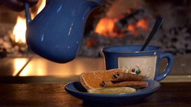 Çay, içki. Bir adam sürahiden çaya, şömine ateşinin arka planına süt döker. Yakın çekim..