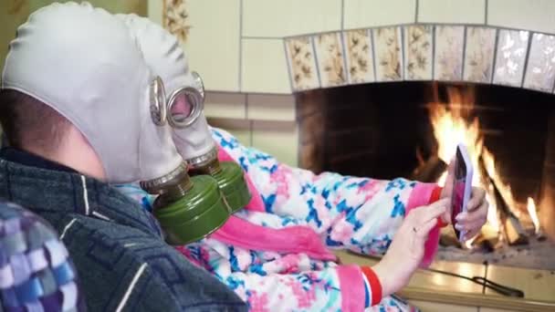 感染症 コヴィト パンデミックの間の女性と男性は ガスマスクで暖炉の近くに座り 電話で自撮りをする クローズアップ撮影 — ストック動画
