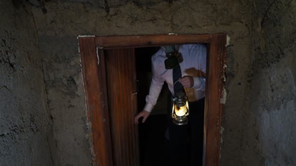 Covid 世界末日后 一个戴着防毒面具 白衬衫 领带和煤油灯的男人打开混凝土地堡中的木门 挥手要进去 — 图库视频影像
