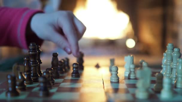 国际象棋 一个孩子和一个成年人的手在壁炉火焰的背景下把这些碎片移动到棋盘上 特写镜头拍摄 — 图库视频影像