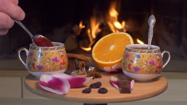 茶话会在壁炉的后面 一个人在一杯茶中放草莓果酱 然后用茶匙搅拌茶 茶的配料 糖果和调味品放在有花瓣的小桌子上 — 图库视频影像