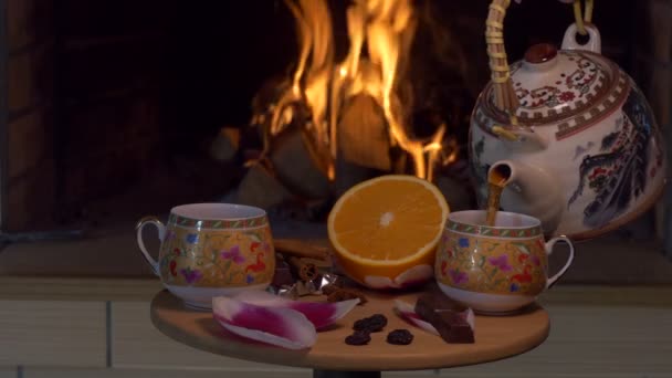 暖炉の炎を背景にテーブルの上に立つカップにお茶を注ぐ人 クローズアップ撮影 — ストック動画