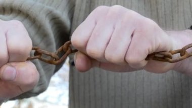Zincir, prangalar. Adam paslı zinciri elleriyle kırmaya çalışıyor. Yakın çekim..
