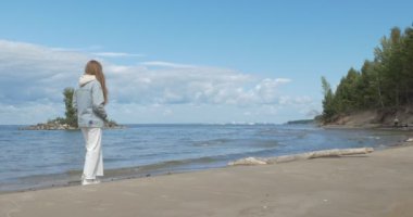 Beyaz elbiseli genç bir kadın kumlu sahil boyunca yürüyor. Ob Nehri, Sibirya.